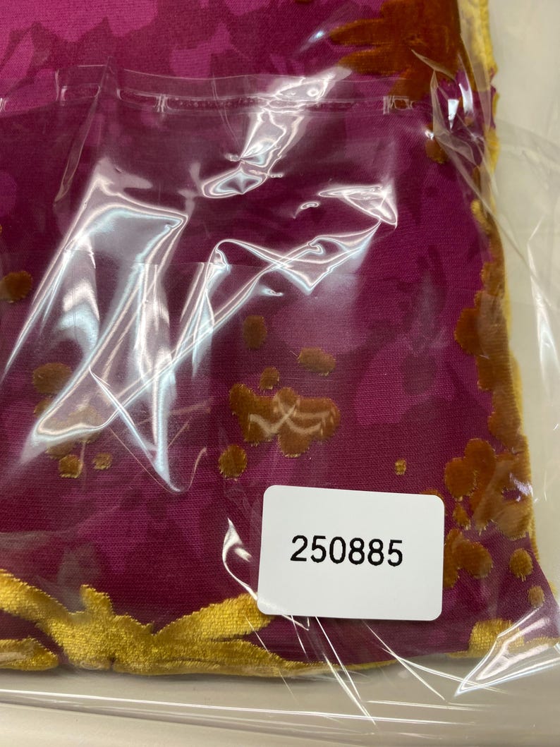 May include: A magenta fabric featuring a raised, textured floral pattern in a golden-brown velvet material. The fabric is encased in a clear plastic protective sleeve with a white rectangular sticker attached, displaying the black printed number 250885.