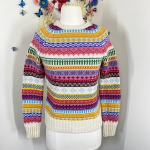 May include: A vibrant, patterned jumper with a round neck. The jumper showcases horizontal bands of diverse colours, including yellow, purple, red, and blue. The cuffs and hem are cream-coloured. The jumper is displayed on a mannequin.