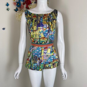 May include: A sleeveless top with a vibrant cityscape design. The top has a scoop neckline and a fitted waist, accentuated by a striped belt. The print showcases buildings, water, and architectural details in blue, yellow, and red hues.