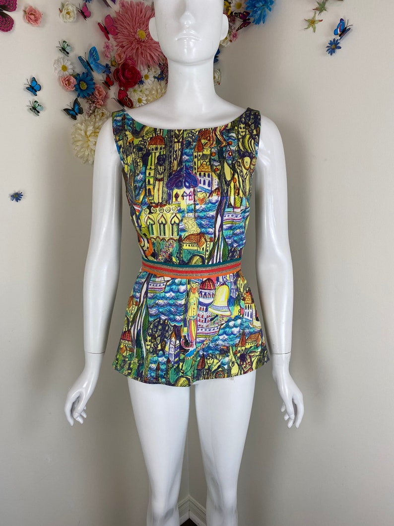 May include: A sleeveless top with a vibrant cityscape design. The top has a scoop neckline and a fitted waist, accentuated by a striped belt. The print showcases buildings, water, and architectural details in blue, yellow, and red hues.