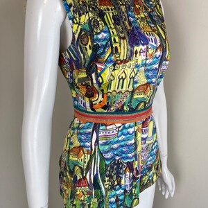 May include: Sleeveless top with a colourful cityscape print. The top features a boat neckline and a fitted waist with a decorative band. The print includes buildings, boats, and water in shades of blue, yellow, green, and purple.