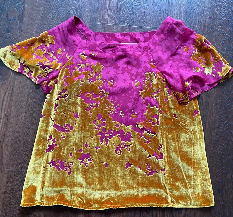 May include: A short-sleeved top featuring a vibrant magenta base with a tonal floral pattern and a contrasting mustard yellow velvet overlay. The velvet fabric is applied in an organic, asymmetrical floral design across the front and sleeves.