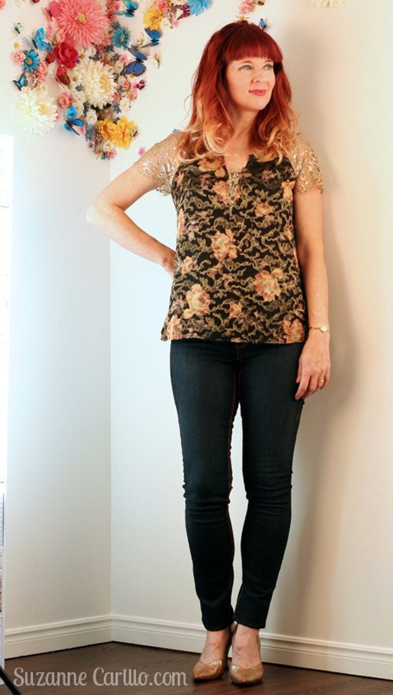 Puede incluir: Una mujer con un top negro con estampado floral y mangas de lentejuelas doradas, combinado con vaqueros azul oscuro y tacones dorados. Decoraci&oacute;n floral en la pared de fondo. Conjunto elegante.