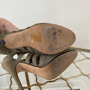 May include: A pair of olive green high-heeled sandals with multiple straps and a stiletto heel. The soles show wear, and the brand name "Valentino" is visible. The size is marked as 36.