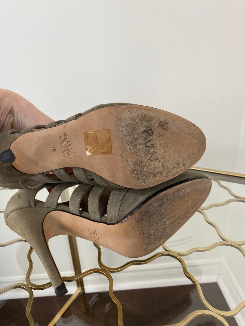 May include: A pair of olive green high-heeled sandals with multiple straps and a stiletto heel. The soles show wear, and the brand name "Valentino" is visible. The size is marked as 36.