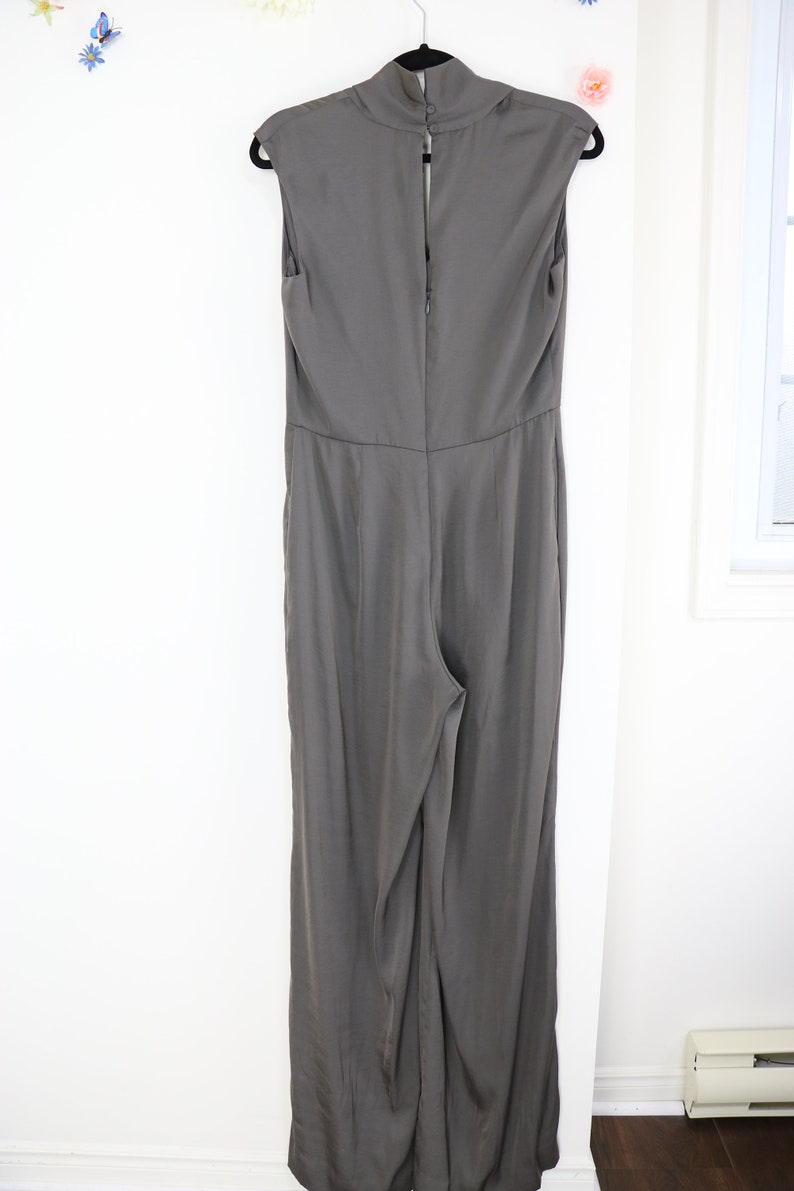 Puede incluir: Mono gris sin mangas con cuello alto, colgado de una percha negra. La parte trasera del mono tiene cierre de cremallera y un bot&oacute;n en el cuello. La tela tiene un brillo sutil.