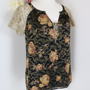Puede incluir: Top negro con estampado floral y mangas de encaje dorado. El top presenta un escote en V con un delicado ribete de cuentas. El estampado floral incluye rosas amarillas y melocot&oacute;n.