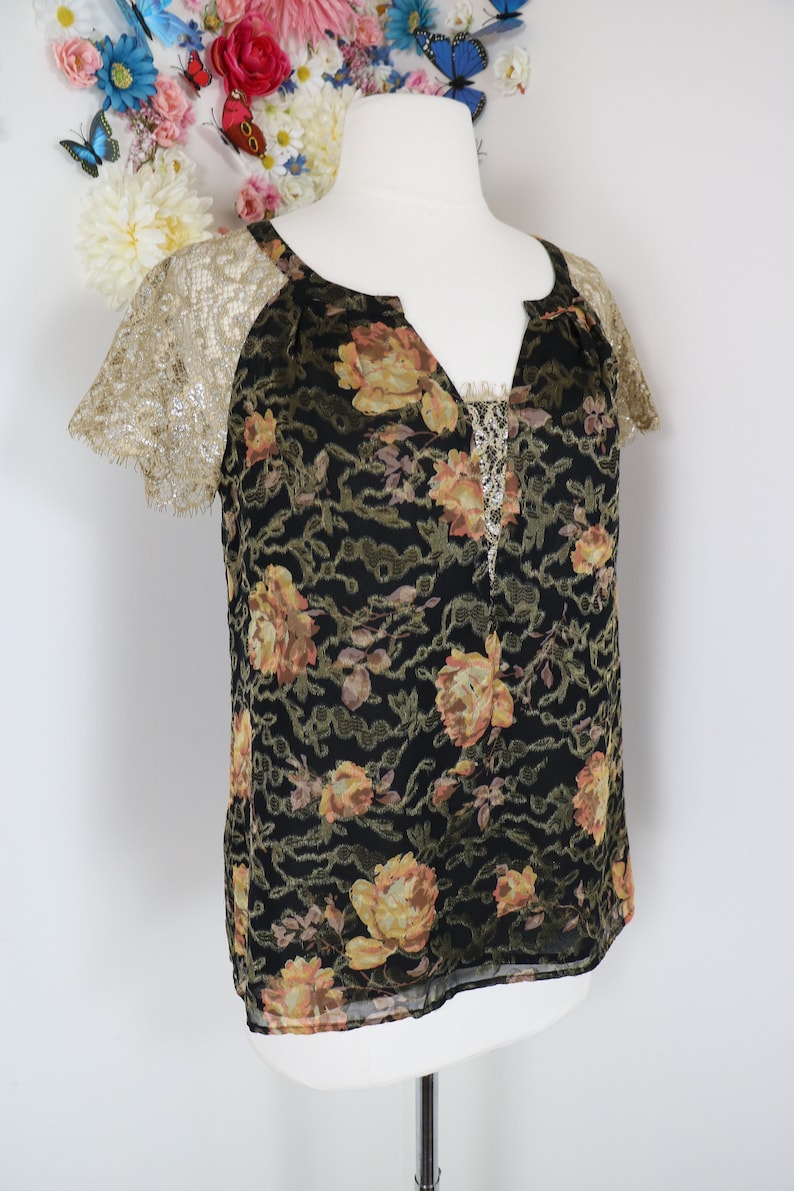 Puede incluir: Top negro con estampado floral y mangas de encaje dorado. El top presenta un escote en V con un delicado ribete de cuentas. El estampado floral incluye rosas amarillas y melocot&oacute;n.
