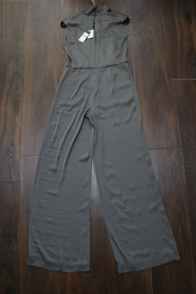 Puede incluir: Mono sin mangas de color verde oliva con cuello alto y perneras anchas. La prenda est&aacute; hecha de una tela suave y cuelga de una percha. Una etiqueta de precio est&aacute; adjunta.