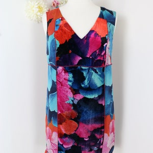 Pode incluir: Vestido sem mangas com decote em V, apresentando um vibrante padr&atilde;o floral em tons de vermelho, rosa, azul e preto. O vestido &eacute; exibido em um manequim sobre um fundo branco, mostrando seu design colorido.