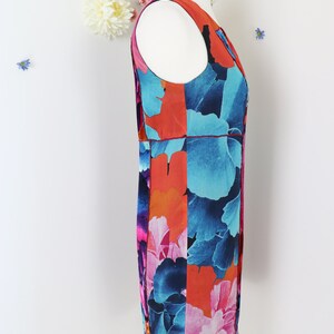 Pode incluir: Vestido sem mangas com um padr&atilde;o floral arrojado em tons de azul, laranja e rosa. O vestido &eacute; apresentado num manequim, destacando o seu design. Tem um decote redondo e um corte reto.