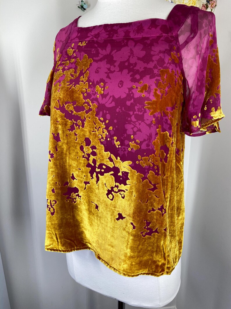 May include: A short-sleeved top featuring a square neckline and a vibrant floral pattern. The garment is constructed from a combination of magenta sheer fabric and textured mustard yellow velvet, creating a distinct contrast in both color and material.