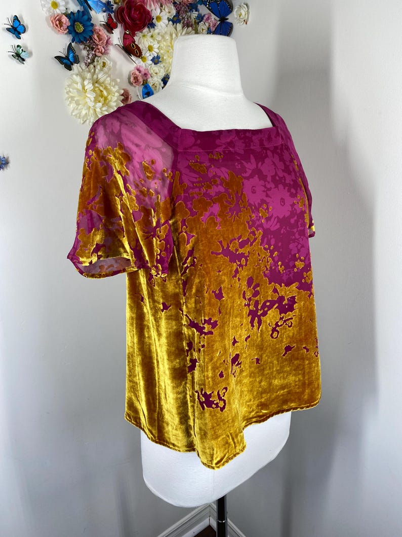 May include: A short-sleeved top featuring a square neckline and a two-tone design. The garment is crafted from a velvet-textured fabric with a floral pattern, transitioning from a deep magenta color at the top to a rich mustard gold at the bottom.