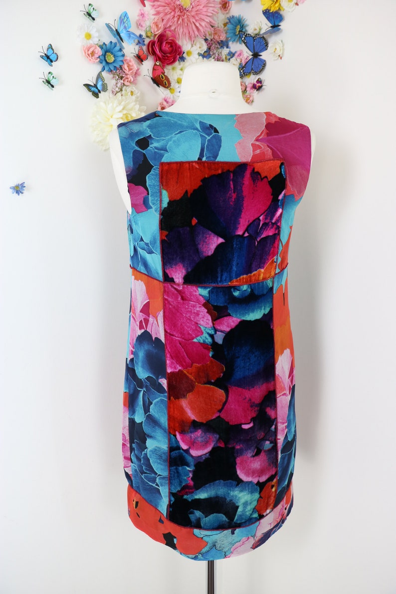Pode incluir: Vestido sem mangas com um padr&atilde;o floral vibrante em tons de azul, rosa e laranja. O vestido apresenta um design de patchwork com uma estampa arrojada e colorida. O vestido &eacute; exibido em um manequim, mostrando sua forma e design.