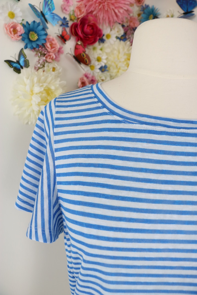 May include: A blue and white striped t-shirt with short sleeves. The shirt is displayed on a mannequin. The background features a collection of colorful flowers and butterflies.