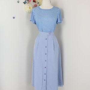 May include: A blue and white striped short-sleeve top paired with a light blue gingham button-down skirt. The skirt has a high waist and is buttoned down the front. The outfit is displayed on a mannequin.