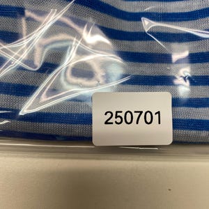 May include: Close-up of a blue and white striped fabric, partially obscured by clear plastic. A white label with the number "250701" is visible.