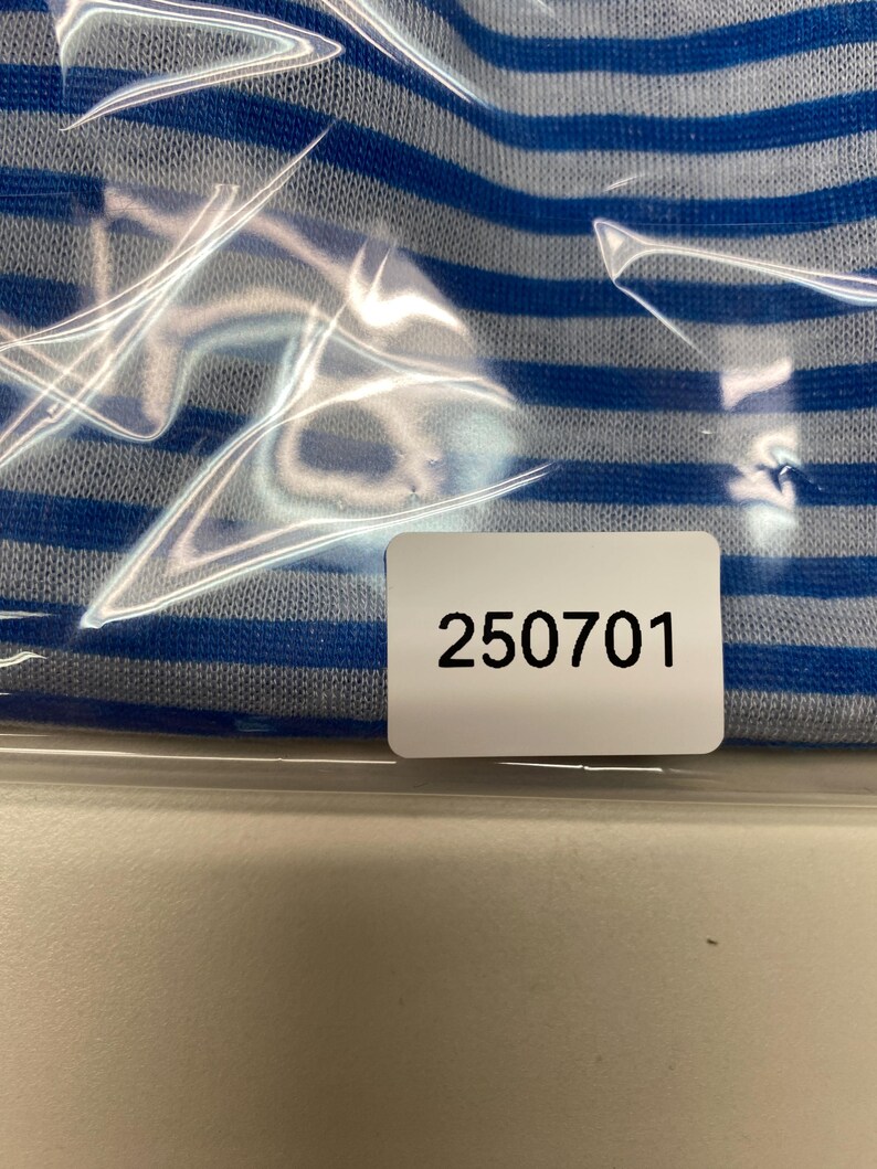 May include: Close-up of a blue and white striped fabric, partially obscured by clear plastic. A white label with the number "250701" is visible.