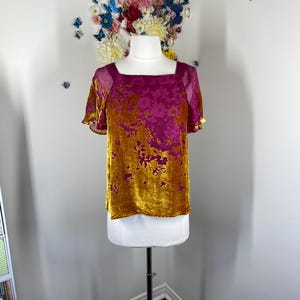 May include: A short-sleeved top featuring a square neckline and a two-tone floral pattern. The garment is crafted from a velvet-textured fabric in shades of deep magenta and mustard yellow, with sheer fabric panels at the shoulders and sleeves.