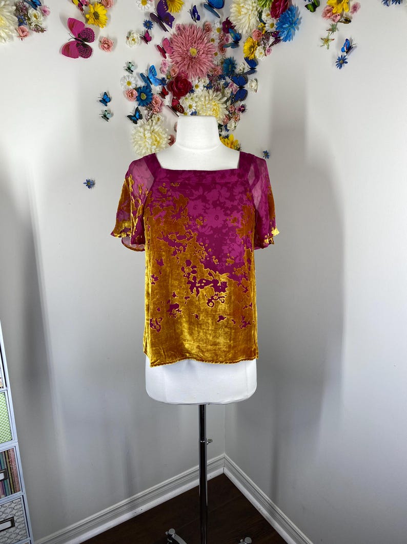 May include: A short-sleeved top featuring a square neckline and a two-tone floral pattern. The garment is crafted from a velvet-textured fabric in shades of deep magenta and mustard yellow, with sheer fabric panels at the shoulders and sleeves.