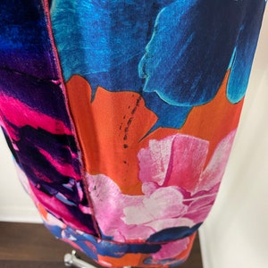 Pode incluir: Um vestido vibrante com estampa floral com grandes flores estilizadas em tons de azul, rosa e laranja. O tecido parece leve, com uma costura vis&iacute;vel no centro. O vestido &eacute; exibido em um manequim prateado.