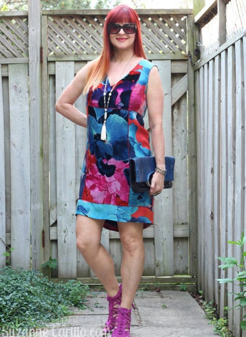 Pode incluir: Um vestido sem mangas, na altura do joelho, com um padr&atilde;o floral vibrante em tons de azul, rosa e vermelho. O vestido &eacute; combinado com uma clutch azul escuro e saltos magenta. Um colar comprido com uma borla branca tamb&eacute;m &eacute; vis&iacute;vel.