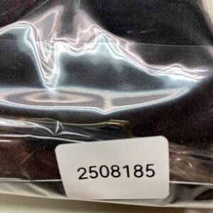 May include: A black item is sealed inside a clear plastic bag. A white sticker with the number "2508185" is visible on the bag.