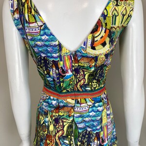 May include: A sleeveless top with a V-neck and a vibrant, artistic print. The design includes boats, buildings, and figures in blue, yellow, and green. A thin, striped band defines the waist.