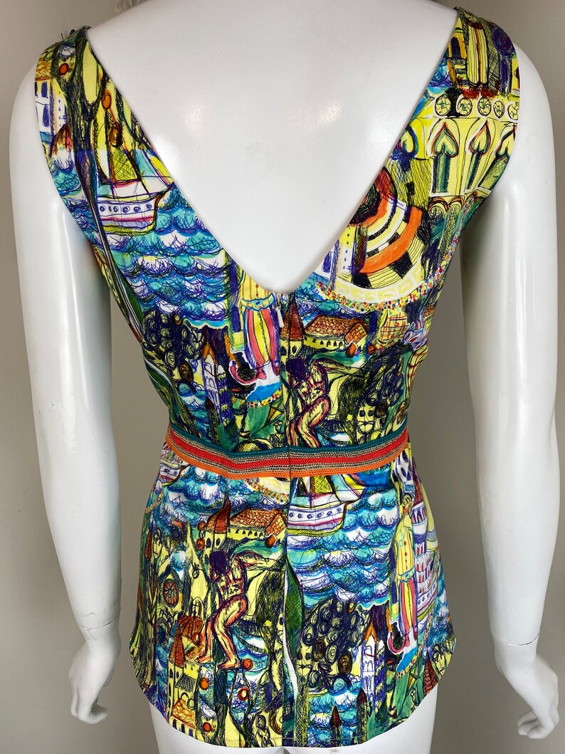 May include: A sleeveless top with a V-neck and a vibrant, artistic print. The design includes boats, buildings, and figures in blue, yellow, and green. A thin, striped band defines the waist.