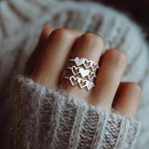 May include: A set of three silver rings, each featuring a heart design. The rings are stacked on a finger, showcasing the intricate heart cutouts. The rings are a simple yet elegant accessory.