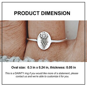 May include: A silver ring with an oval pendant displaying a floral design. The oval pendant is 0.76 cm by 0.61 cm, with a thickness of 0.13 cm. The text "PRODUCT DIMENSION" is at the top. The ring is shown on a finger.