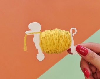 May include: A white plastic yarn holder shaped like a dog holding a ball of yellow yarn.