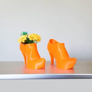 May include: Two bright orange high-heeled shoes, one with a bouquet of yellow flowers in the top, used as a planter.