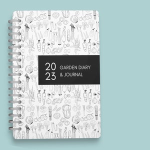 Pu&ograve; includere: Un diario bianco a spirale con un'illustrazione in bianco e nero di verdure sulla copertina. Il diario &egrave; intitolato "2023 Garden Diary & Journal".