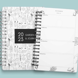 Pu&ograve; includere: Un diario a spirale bianco e nero con una copertina che presenta un motivo di verdure disegnate a mano. La copertina ha anche un'etichetta nera con il testo "2023 GARDEN & JOURNAL". Le pagine interne sono vuote e presentano un calendario per novembre, settimana 47.