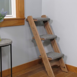 May include: A wooden pet step with three gray carpeted steps. The step is angled and has a wooden base.