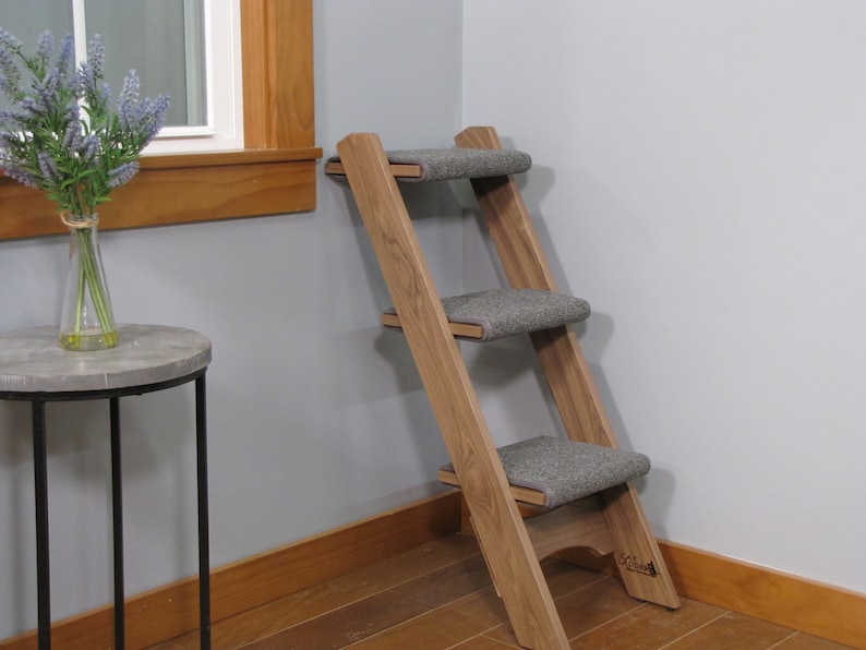 May include: A wooden pet step with three gray carpeted steps. The step is angled and has a wooden base.