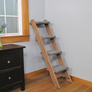 May include: A wooden cat ladder with four steps, each covered in gray carpet. The ladder is angled against a wall and has a natural wood finish.