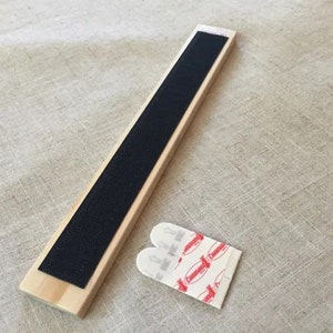 May include: A wooden strip with black adhesive tape on one side and two adhesive strips with red and white markings on the other side.
