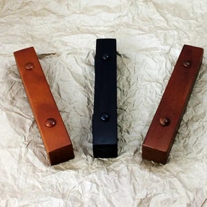 May include: Three wooden rectangular blocks with rounded edges. The blocks are painted in different colors: brown, black, and a lighter shade of brown. Each block has a small black metal knob on each end.