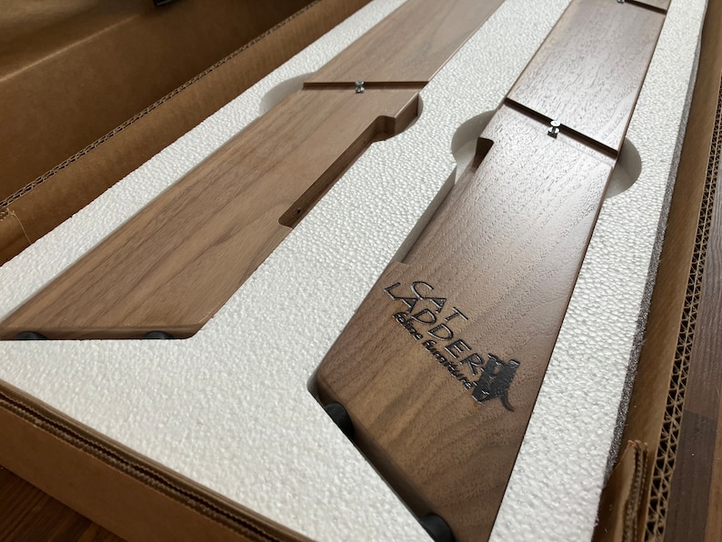 May include: Two wooden cat ladders in a brown cardboard box with white foam padding. The ladder on the right has the text "CAT LADDER" and "Elite Furniture" engraved on it.