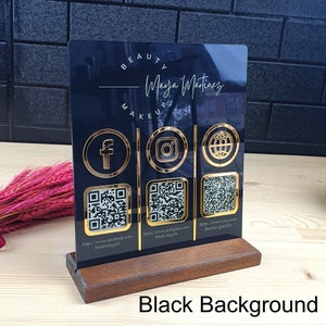May include: A black acrylic business sign with gold accents and a wooden base. The sign features the name "Maya Martinez" and social media icons for Facebook, Instagram, and a website, each with a corresponding QR code. The words "BEAUTY MAKEUP" are at the top.