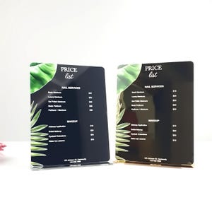 May include: Two black acrylic price lists with a tropical leaf design. The price list includes services for nail care and makeup. The text on the price list reads "PRICE list" and lists prices for services such as basic manicure, luxury manicure, gel polish manicure, basic pedicure, pedicure + manicure, makeup application, bridal makeup, eyelash extensions, and make up lessons.