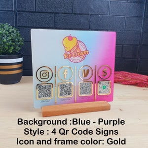 May include: A decorative sign for an ice cream shop with a blue and purple gradient background. It features gold icons for Instagram, Facebook, Venmo, and a payment app, each with a QR code. The sign is mounted on a wooden base.