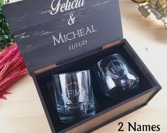 May include: A wooden box with a black finish and engraved with the names "Felicia & Micheal" and the date "11/11/23". The box contains two clear glass tumblers with the initials "FIM" engraved on them.