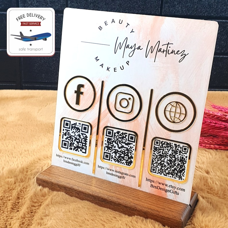 May include: A wooden-based acrylic sign for a beauty business. The sign features the name "Maya Martinez" and social media icons with QR codes for Facebook, Instagram, and Etsy. The background has a pink and white watercolor effect.