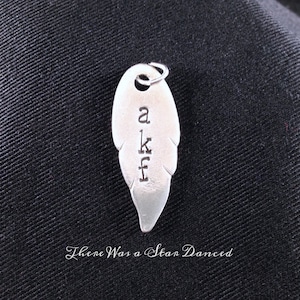 Może przedstawiać: Srebrny zawieszka w kształcie pióra z wygrawerowanymi literami "akf". Zawieszka ma pętelkę na górze do przymocowania do naszyjnika lub bransoletki.