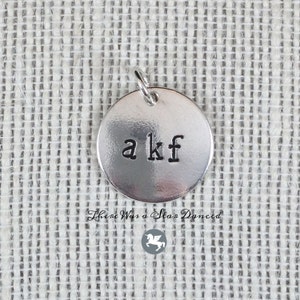May include: A silver charm with the letters "a kf" engraved on it.