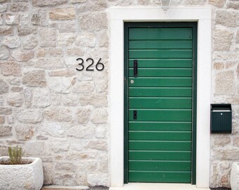 May include: A green wooden door with the number 326 above it, set in a white frame against a stone wall. A matching mailbox is mounted on the wall. Two stone planters with greenery flank the door.