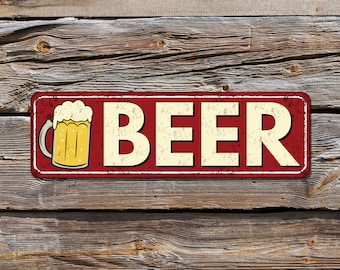 May include: A rectangular metal sign with the word "BEER" in large, off-white letters. A yellow beer mug with white foam is on the left. The sign has a red border and is mounted on a weathered wooden background.